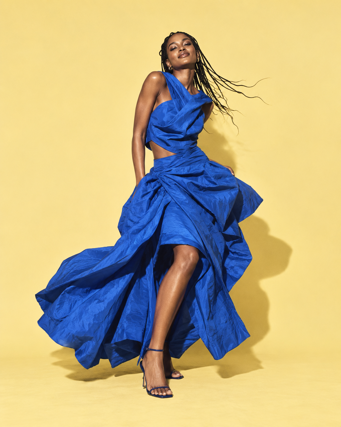 Fashion model wearing a flowing cobalt blue outfit against a yellow studio backdrop